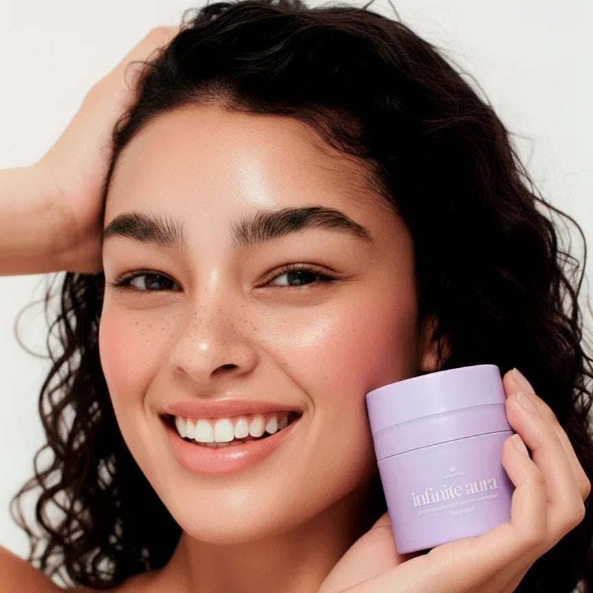 Smiling woman with glowing skin holding Bohemia Skin Infinite Aura moisturizer in lavender jar
