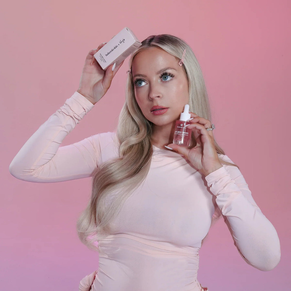 Woman holding Bohemia Skin glow serum and box against a pink background