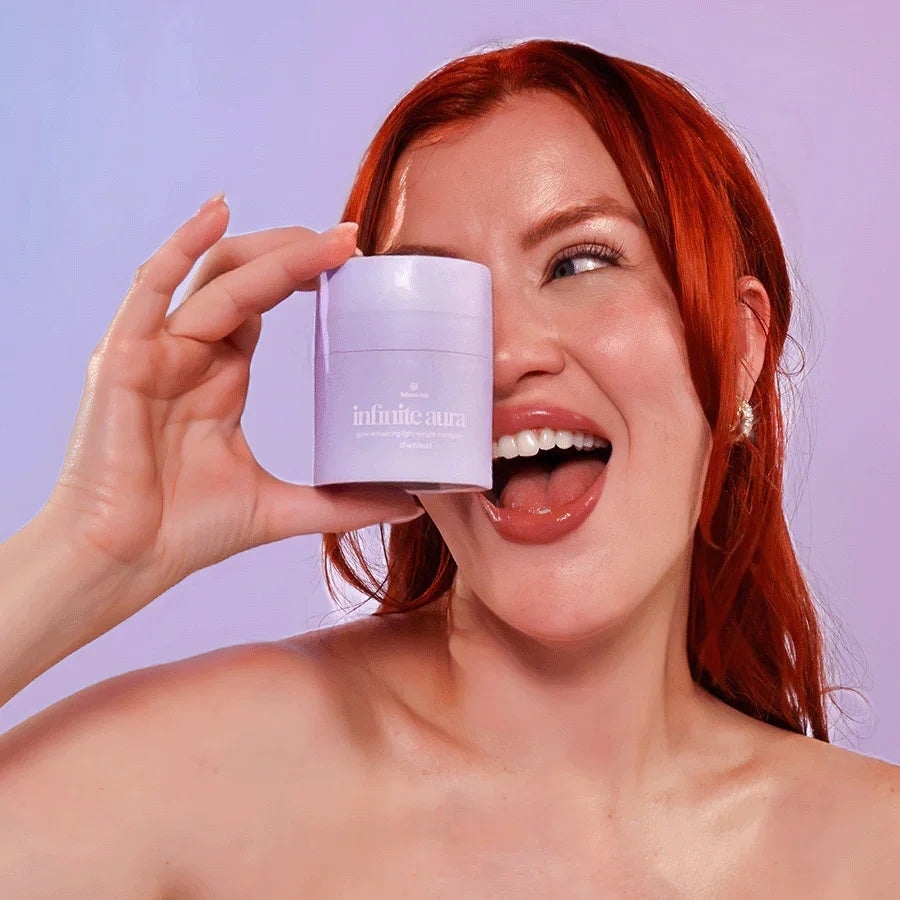 Woman with red hair holding Bohemia Skin Infinite Aura skincare product by her face