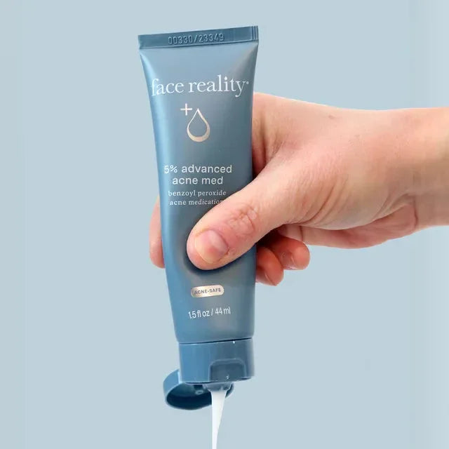 Hand squeezing Face Reality 5% advanced acne medication cream, skincare product on blue background
