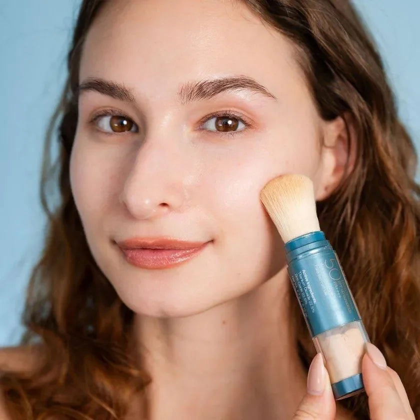 Model brushing Colorescience Sunforgettable Total Protection Brush-On Shield SPF 50 Glow onto her cheek with its brush.