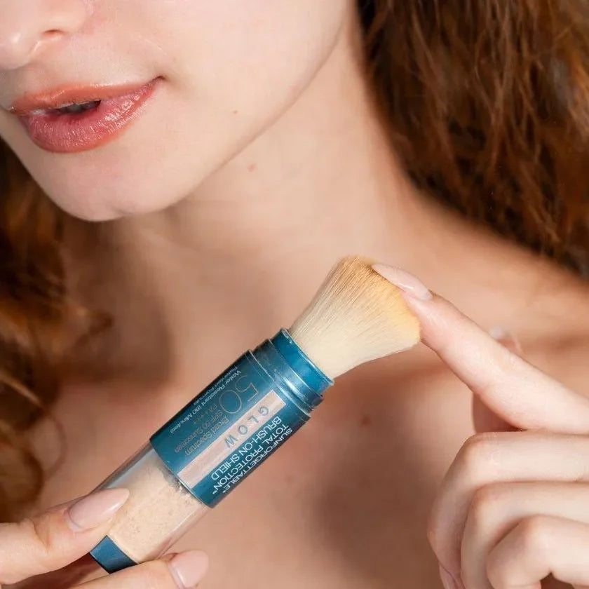 Close-up of a model holding the Colorescience Sunforgettable Brush-On Shield SPF 50 Glow brush near her jaw and neck.