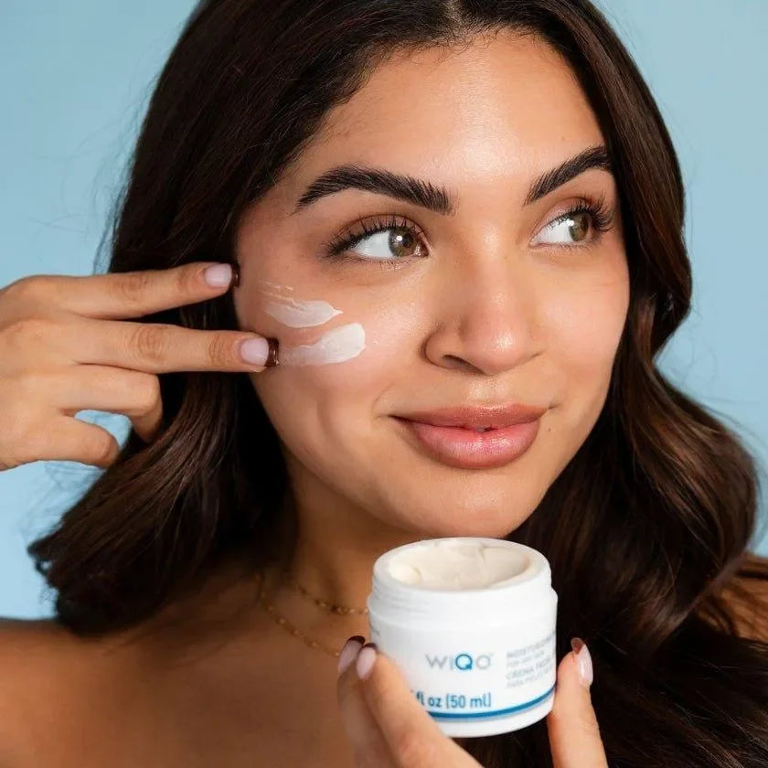 Woman applying WiQo Moisturizing Face Cream For Dry Skin to her cheek while holding the open jar, a model shot.